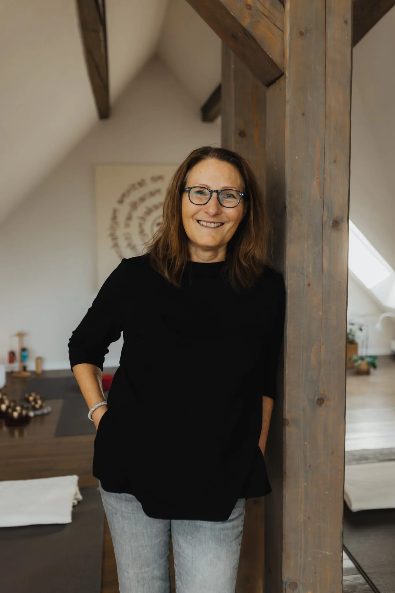 Heike Lenz lehnt lächelnd an einem Holzbalken im Yogastudio