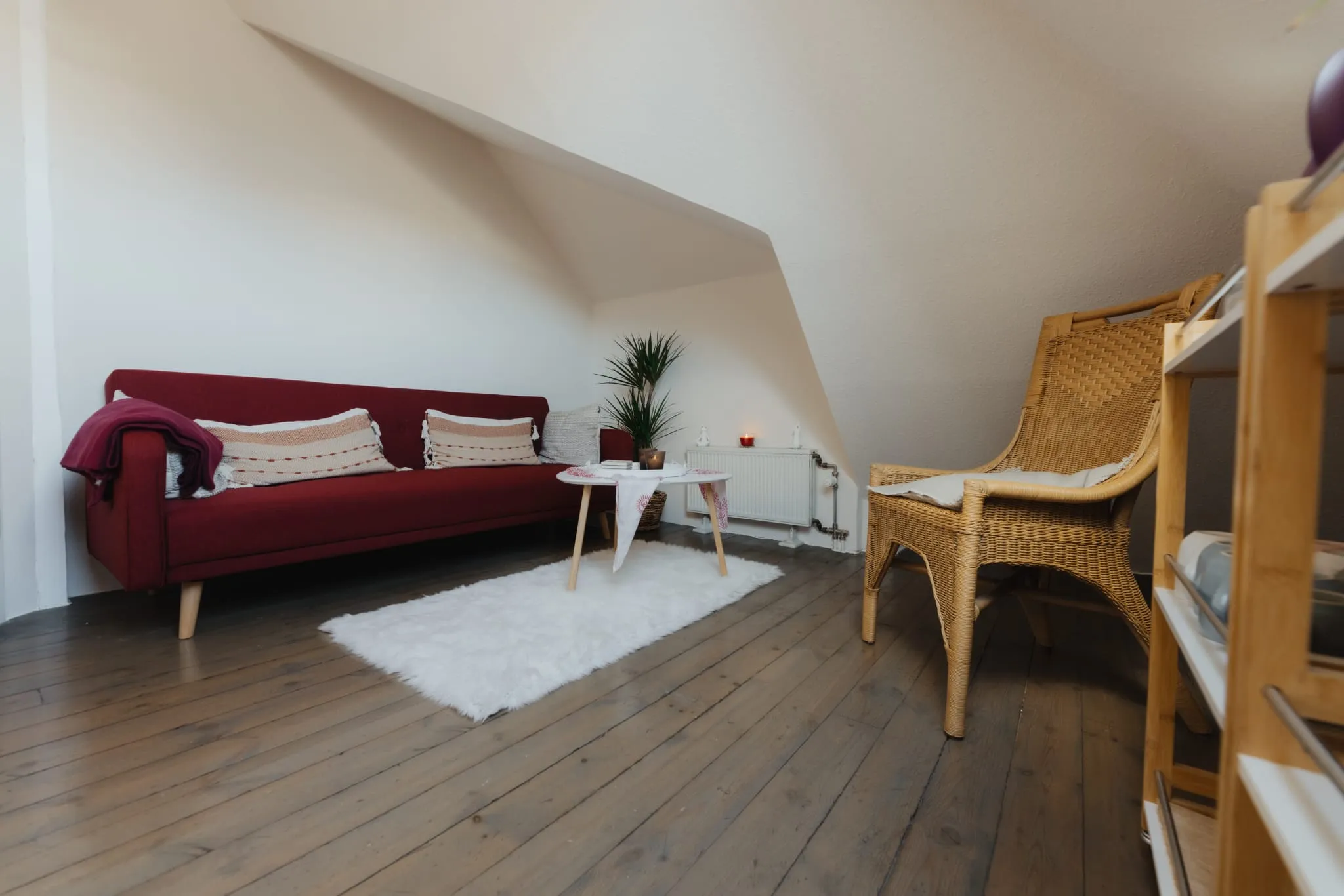 Ruhebereich mit rotem Sofa, Korbsessel und Pflanze unter der Dachschräge