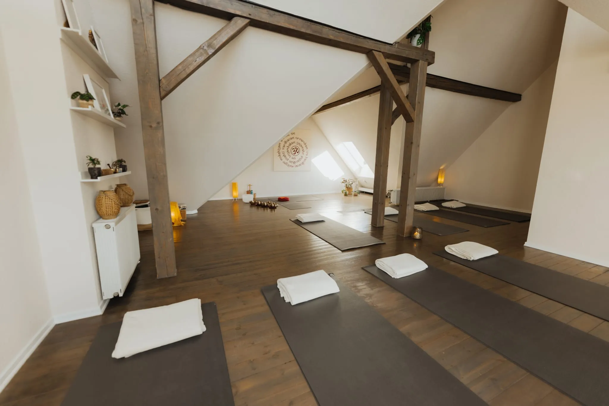 Yogaraum mit Holzbalken, Matten, Decken und Kerzen, an der Wand ein Mandala
